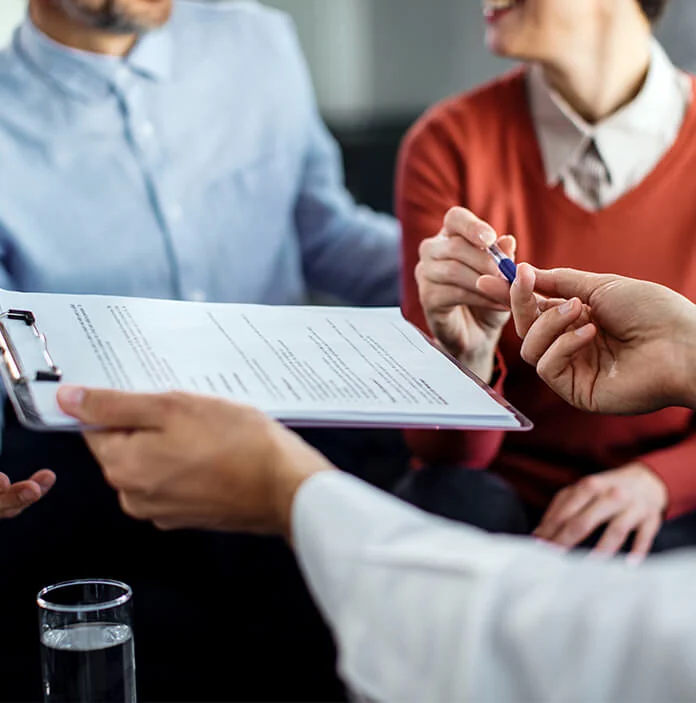People reviewing a document together over a clipboard, one handing across a pen